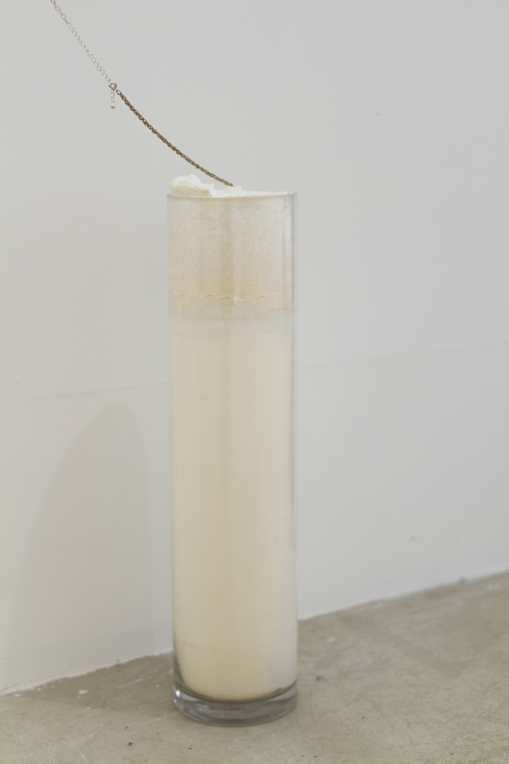 A glass column filled with white wax with delicate charms and chains attached to it